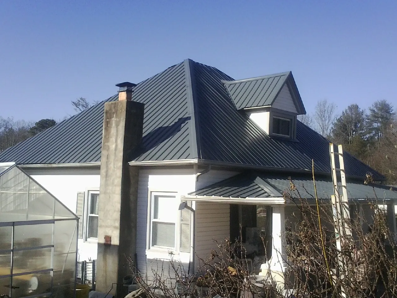 Dark blue standing seam metal roof on a white farmhouse with dormer — Slate & Tile Roof Repair by Roofing Brothers in Egan