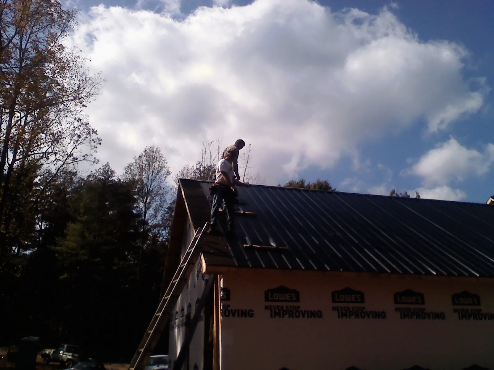 Roofer fastening dark metal panels high against a cloudy sky, from a Roof Inspection job in Egan