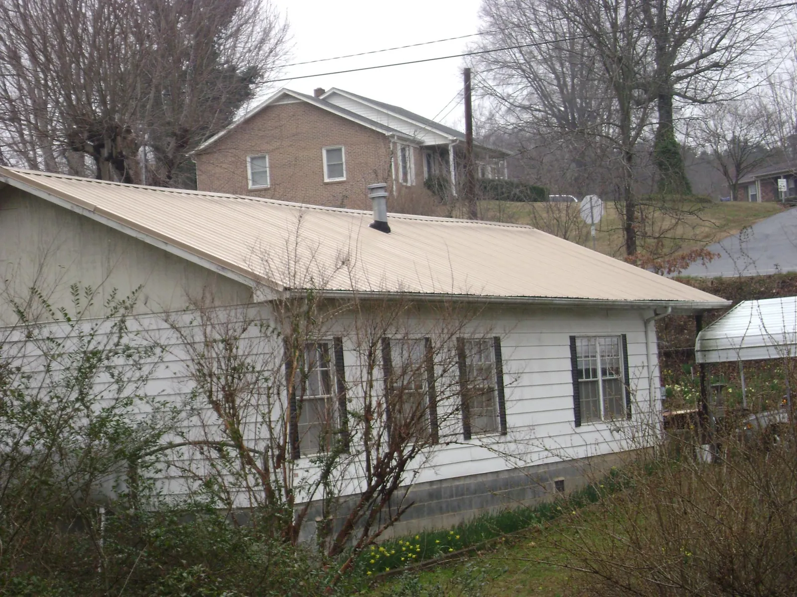 Tan metal roof on a white sided house set into a hillside — Commercial Roofing by Roofing Brothers in Egan