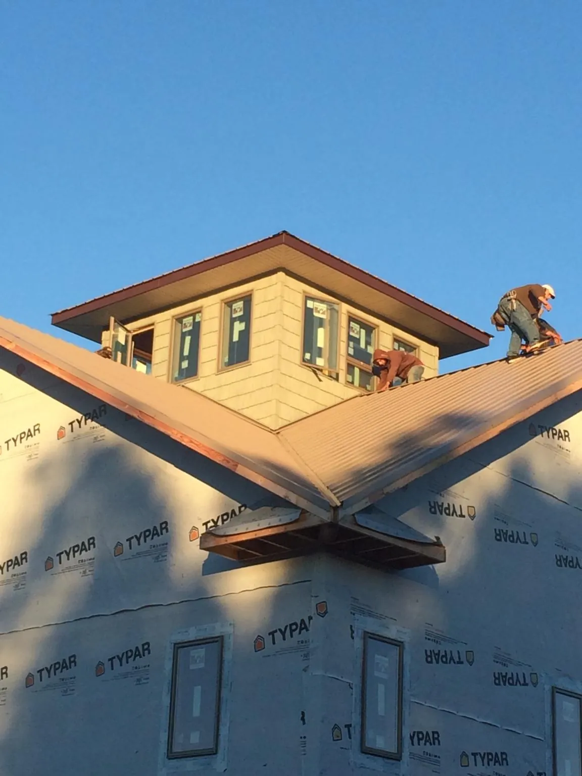 Roofers working around a rooftop cupola on a new metal roof at sunset — Roof Waterproofing in Egan by Roofing Brothers